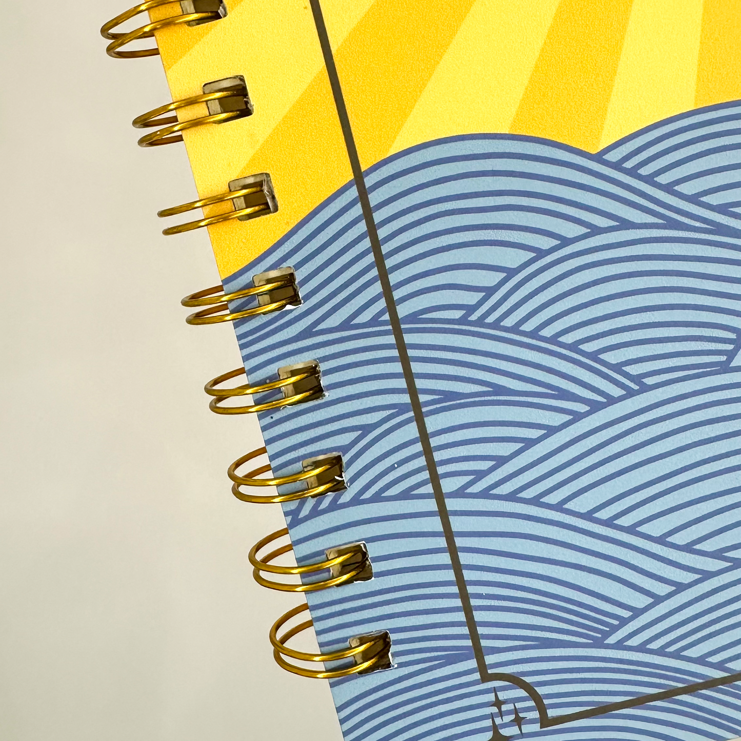 Notebook with spiral binding, yellow sun design, and blue wave pattern on white background
