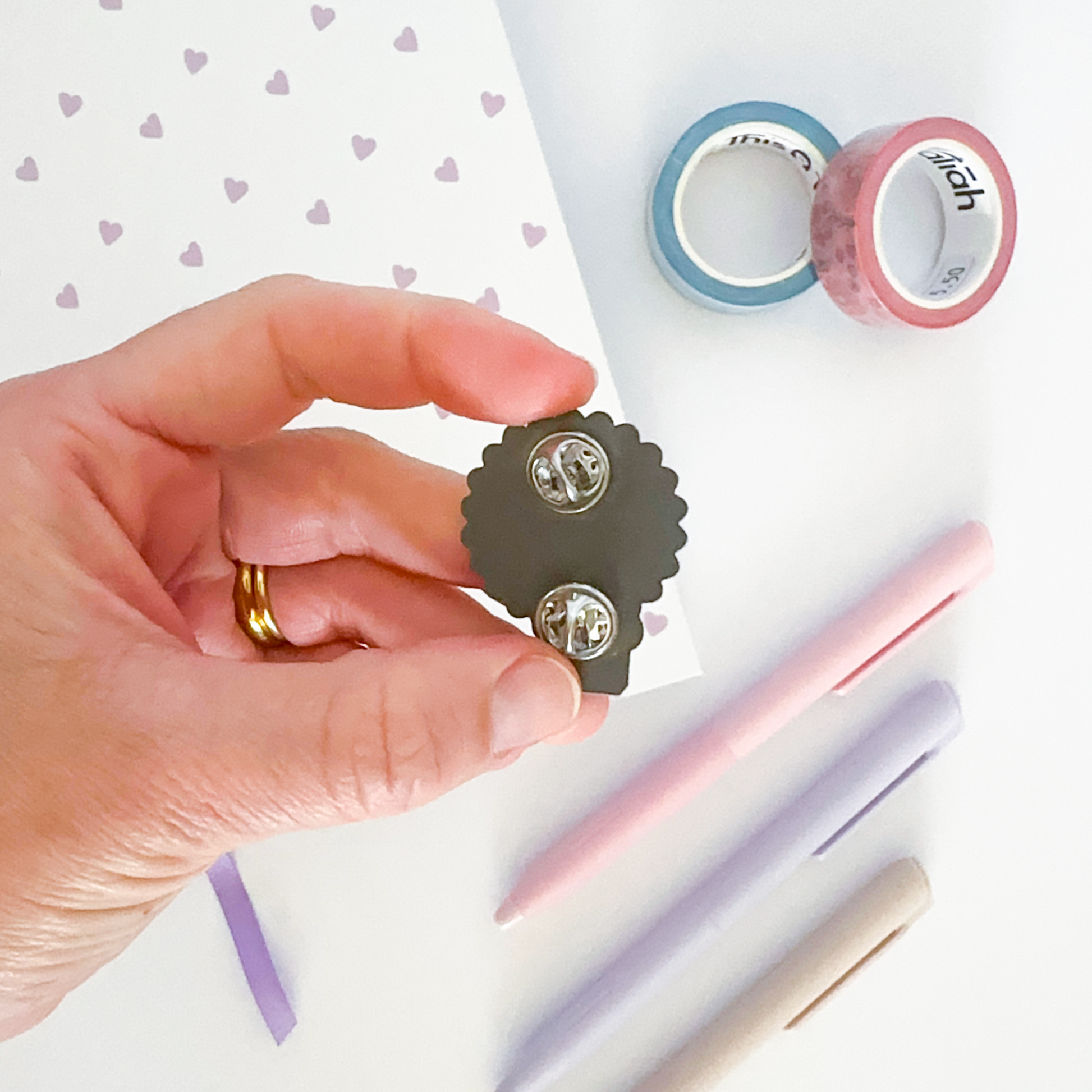 Enamel pin with notebook, coloured pen and washi tapes in the background