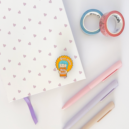 Enamel pin with notebook, coloured pen and washi tapes in the background