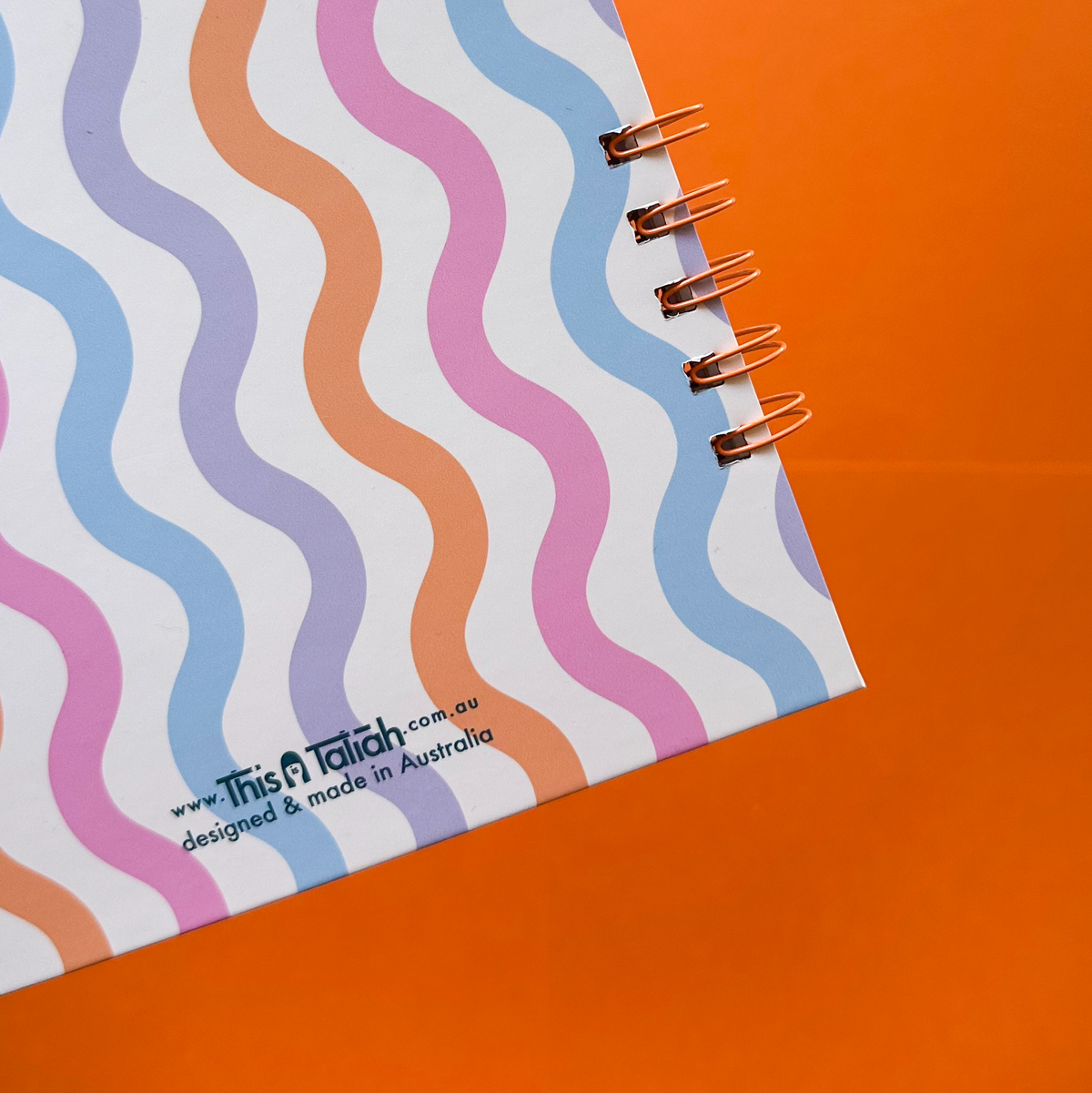 Showing corner from back cover of planner, with pastel curvy lines blue, orange, purple and pink in a orange background.