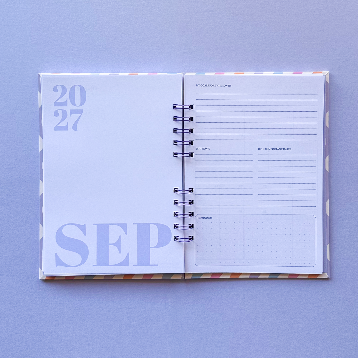 An open spiral-bound planner or agenda showing September 2027, laid flat on a light lavender background. The left page displays '2027 SEP' in light purple, and the right page contains lined writing sections and a small grid box.