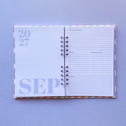An open spiral-bound planner or agenda showing September 2027, laid flat on a light lavender background. The left page displays '2027 SEP' in light purple, and the right page contains lined writing sections and a small grid box.