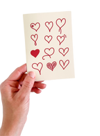 Hand holding a card with red heart designs on a white background