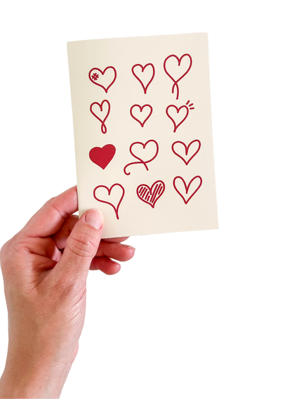Hand holding a card with red heart designs on a white background