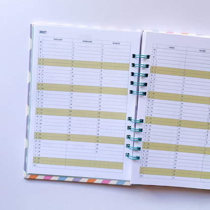 An open spiral-bound planner or agenda showing printed weekly planning pages with light yellow highlighted sections, photographed on a plain white background.
