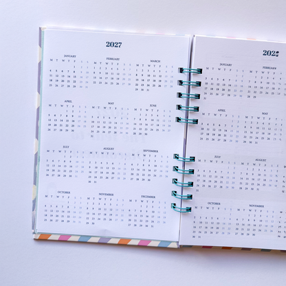 An open spiral-bound planner or calendar showing the 2027 monthly calendar pages, photographed from above on a plain white background.